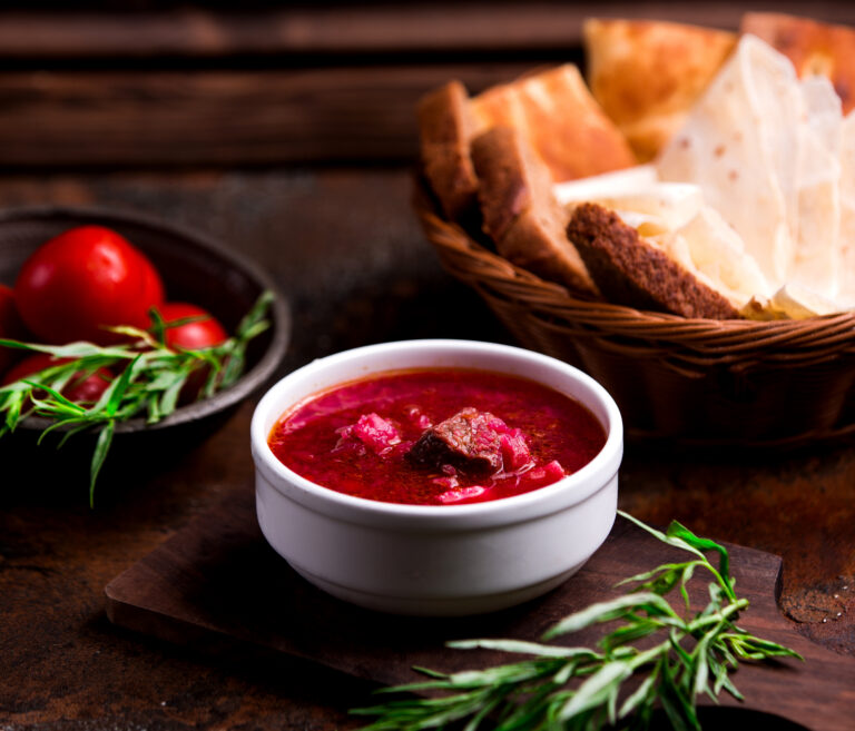 a bowl of borsch with meat, slices of rye bread and baked pork